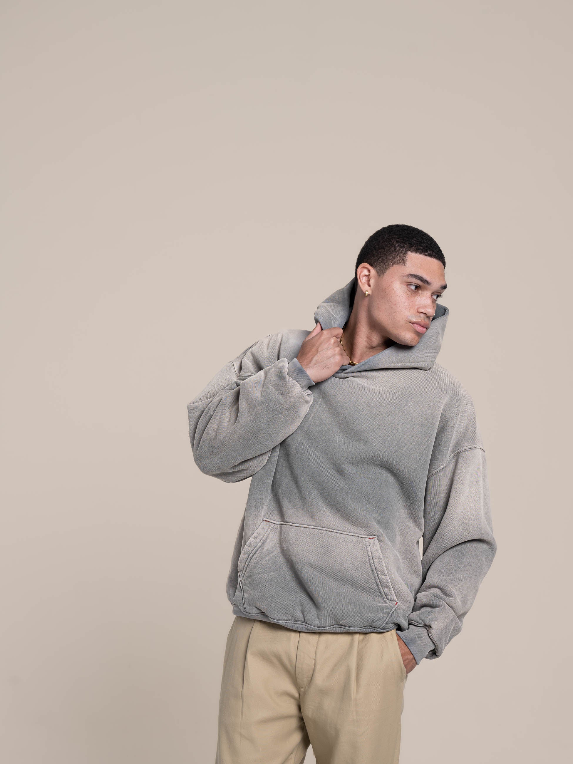 male model holds neck line of the double layered fleece ash blue hoodie