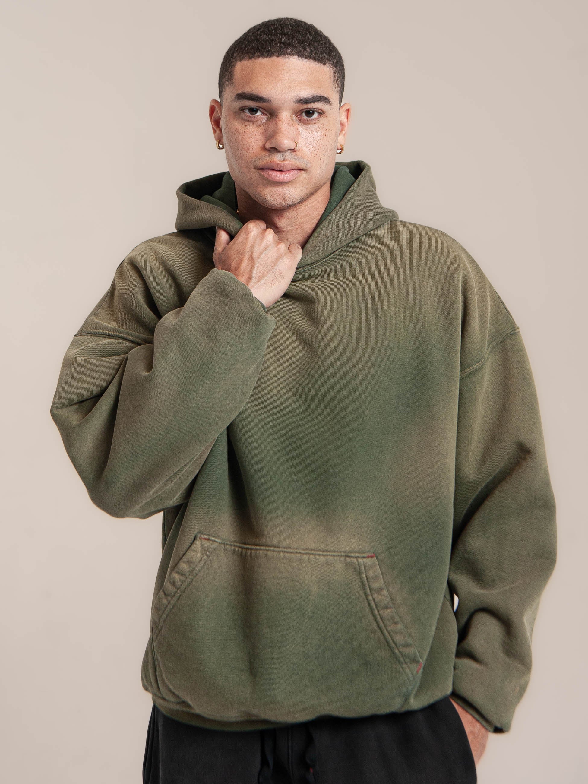 male model wears Publik Brand Double Layered Hoodie Reseda Green Heavyweight Fleece, all made in USA, holding hood neck line