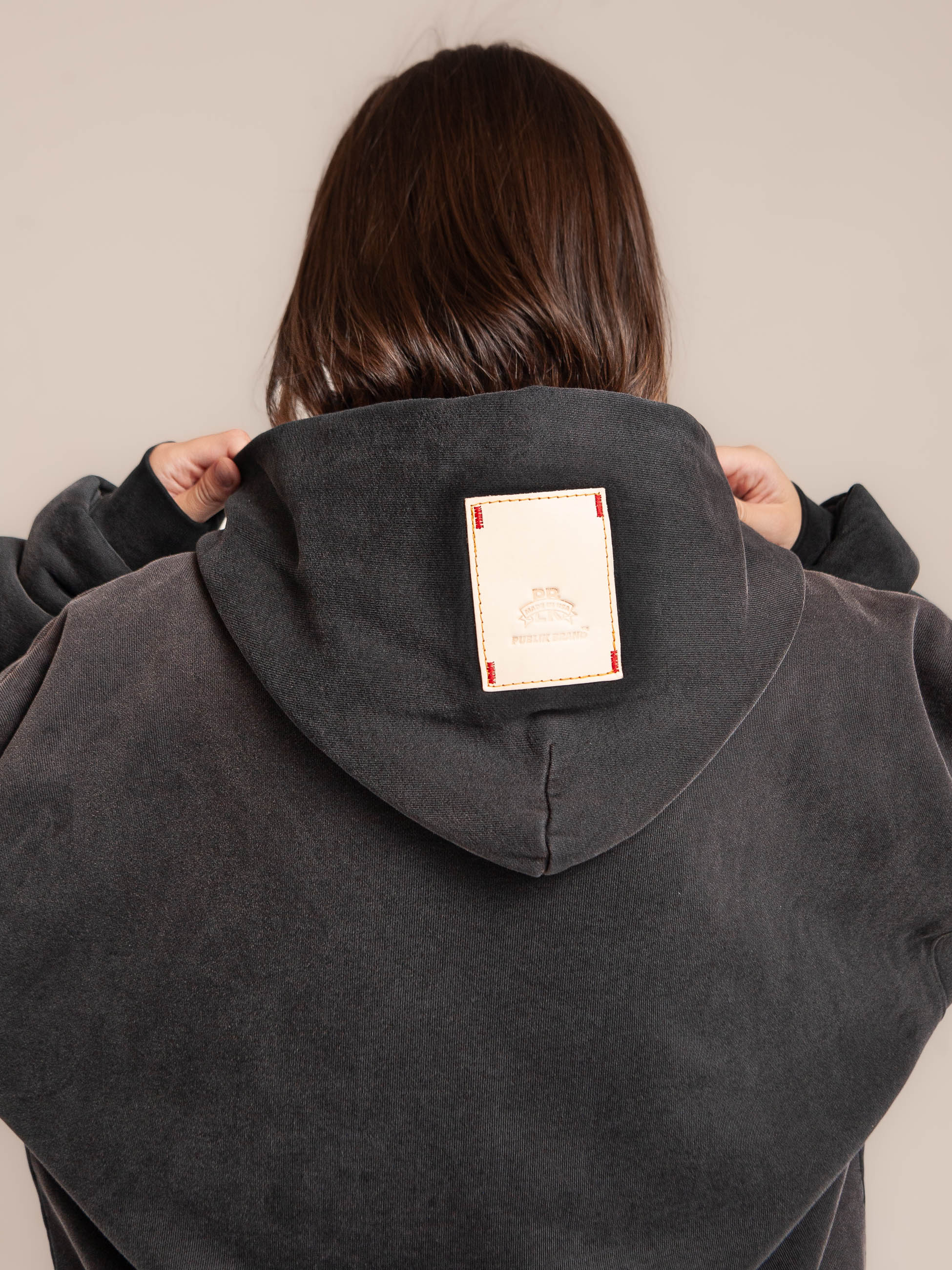 Female model shows Publik Brand leather patch logo on the black hood Double Layered Fleece Black Hoodie Flat Luxury Made in USA